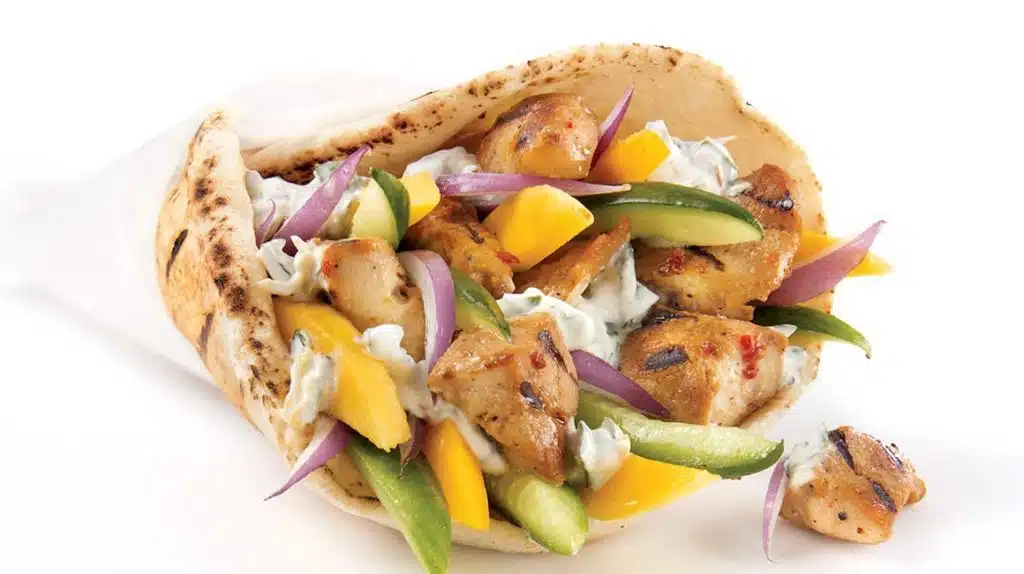 Photo of a traditional Greek Chicken Souvlaki in a white paper cone with colorful vegetables, grilled chicken and pita bread on a white background