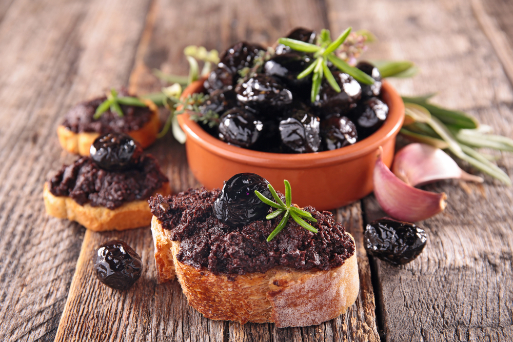 Black olive tapenade on toasted bread with whole olives and fresh herbs