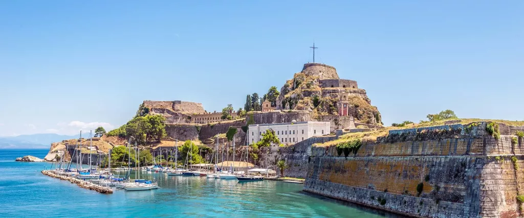 Corfu port with fortress, fort with cross, boats, sailboats, pleasure boats, sea and mountains in the distance