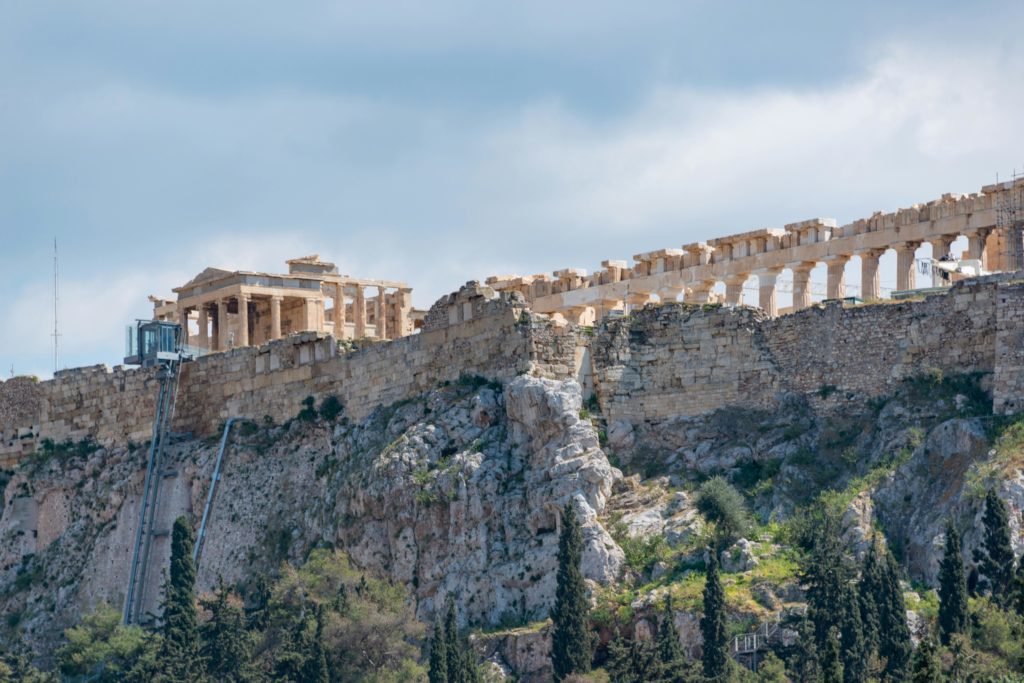 Άποψη της Ακρόπολης των Αθηνών με τον Παρθενώνα σε βραχώδη λόφο κάτω από συννεφιασμένο ουρανό. Growy and Tasty