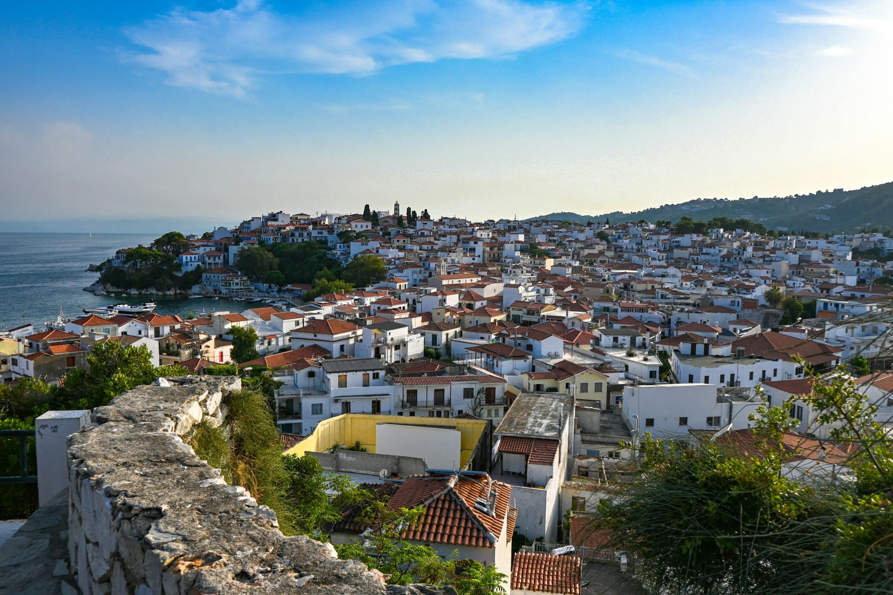 Village de Skiathos en Grèce avec maisons blanches à toits rouges, collines verdoyantes et mer en arrière-plan