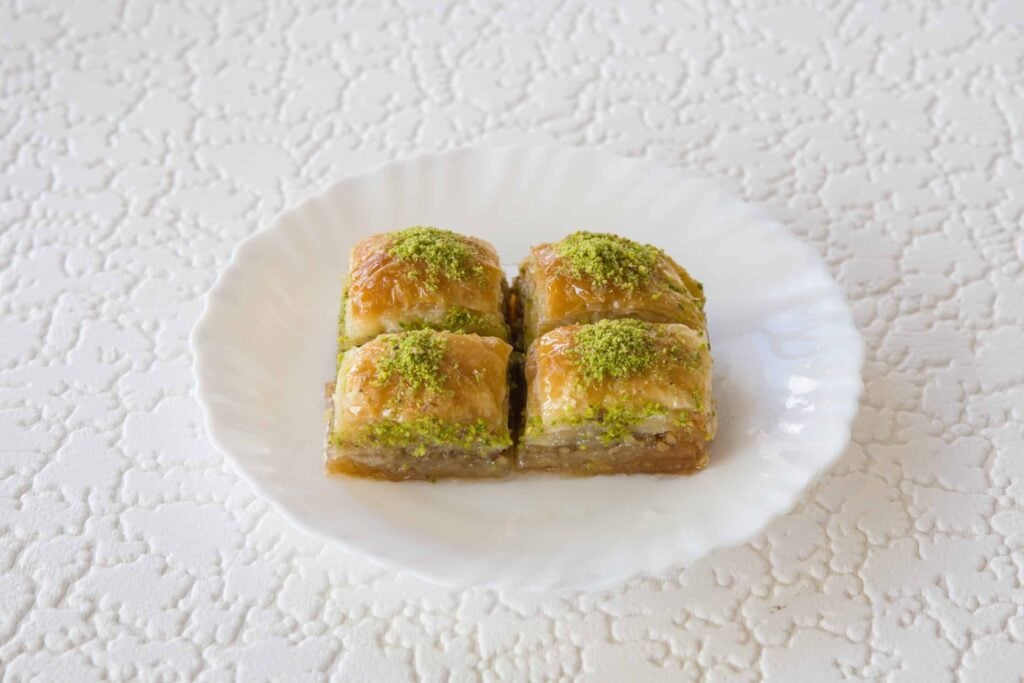 Baklava grec traditionnel aux noix et pistaches, servi en portions sur une assiette blanche.