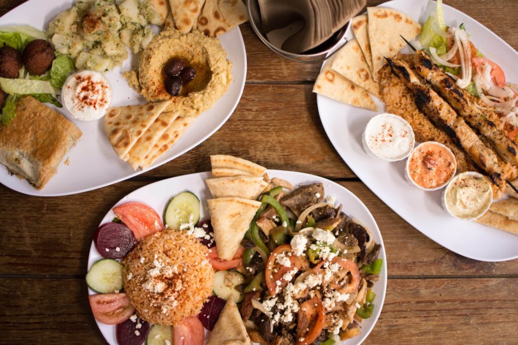 Assortiment de plats grecs traditionnels avec pita, houmous, brochettes et légumes frais.