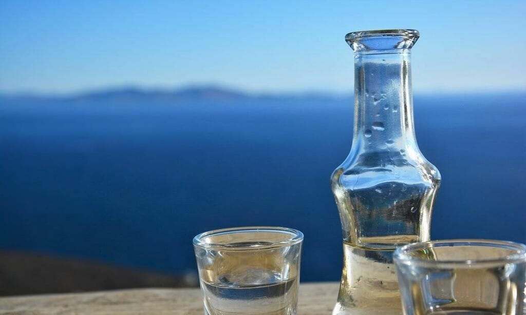 Verre de Tsikoudia servi avec une vue panoramique sur la mer, capturant l’essence de la Crète.