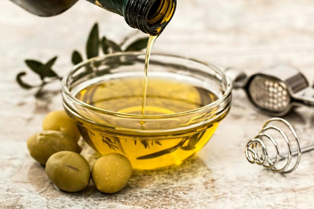 Greek olive oil poured into a bowl with fresh green olives alongside.