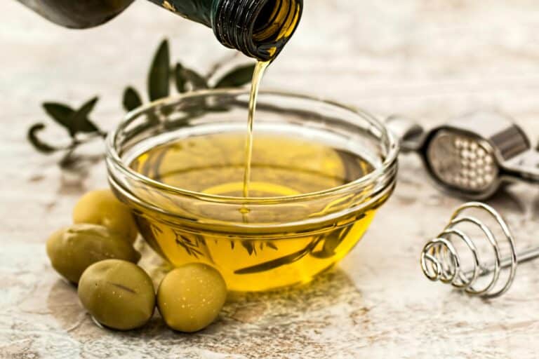 Greek olive oil poured into a bowl with fresh green olives alongside.