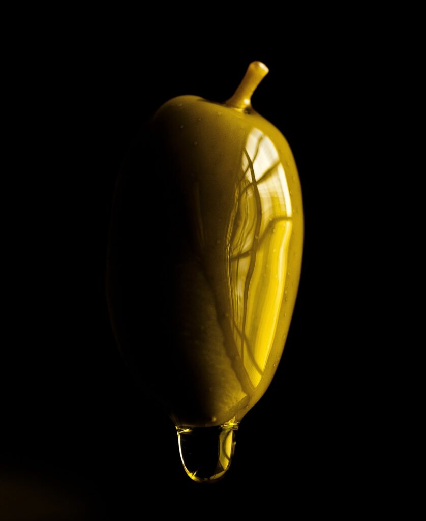 A drop of Greek olive oil falling from a green olive.