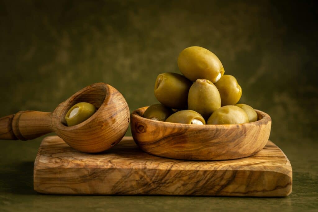 Green olives served in bowls with a Greek olive wood spoon.