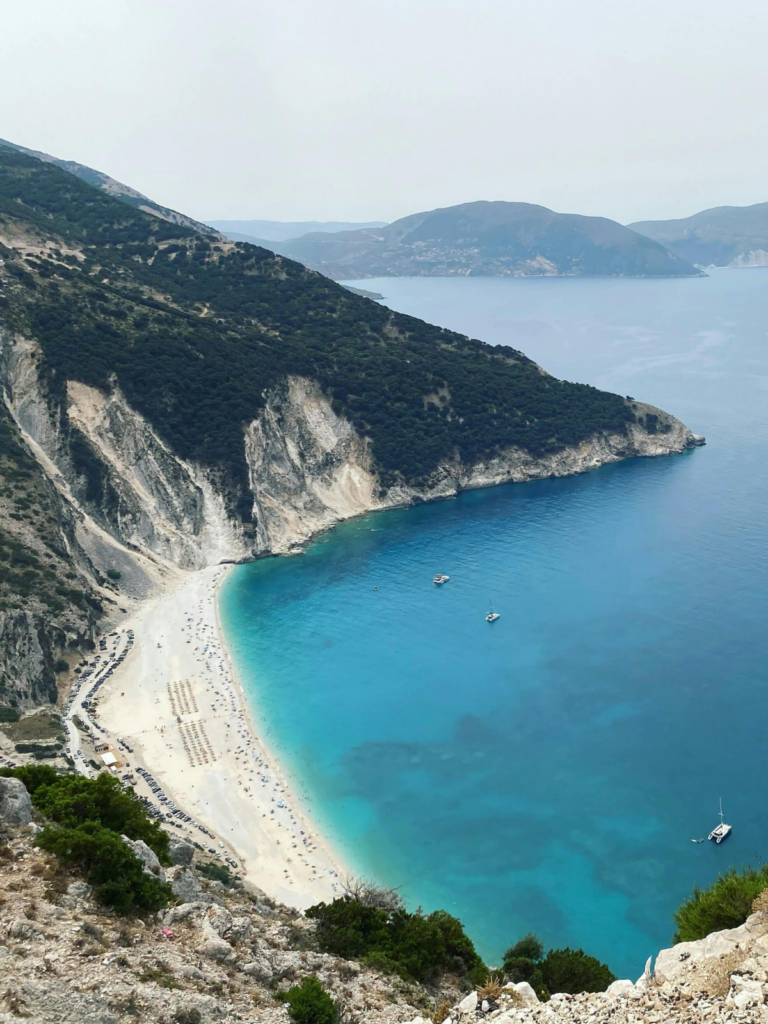 Plage de sable blanc et mer turquoise à Céphalonie avec falaises et voiliers