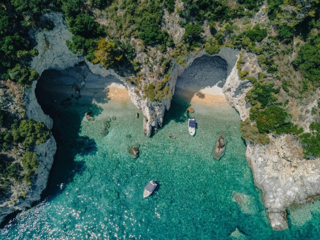 Vue aérienne d’une plage secrète à Zakynthos avec mer turquoise et petites embarcations, idéale pour visiter Zakynthos.