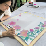 Συμμετέχουσα ζωγραφίζει ένα μεταξωτό μαντήλι με ροζ λουλούδια σε εργαστήριο τέχνης στην Αθήνα