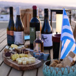 Primo piano di un tavolo di degustazione con vini greci, raki, mezzeseghe e formaggi su una terrazza con vista su Chania, Creta.