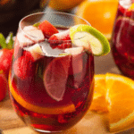 Verre de sangria aux fruits frais, avec tranches d’orange, citron vert et fraises, sur planche en bois.