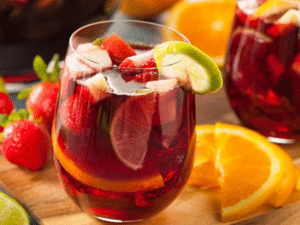 Verre de sangria aux fruits frais, avec tranches d’orange, citron vert et fraises, sur planche en bois.