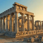 Temple antique d’Égine au coucher du soleil, avec colonnes doriennes et ciel doré.