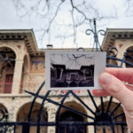 Personne tenant une photo vintage devant un bâtiment historique à Athènes, capturant l’art et l’architecture de la ville.
