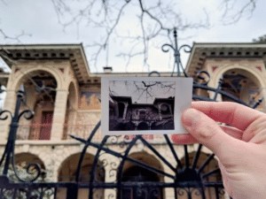 Personne tenant une photo vintage devant un bâtiment historique à Athènes, capturant l’art et l’architecture de la ville.