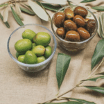 Coupes d'olives vertes et noires prêtes à la dégustation, accompagnées de branches d'olivier, représentant la tradition grecque.